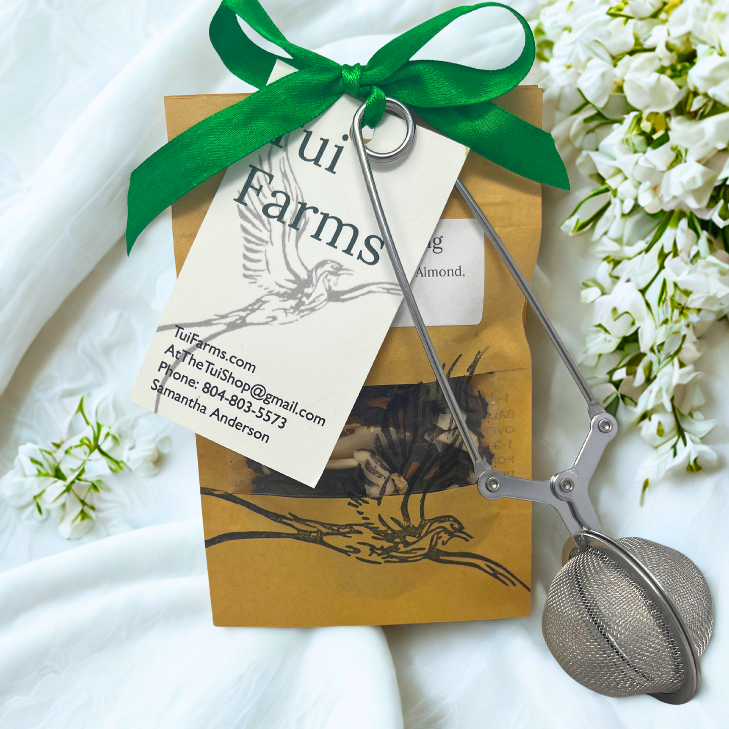 Tea bag with a green ribbon and tea strainer on a white fabric background